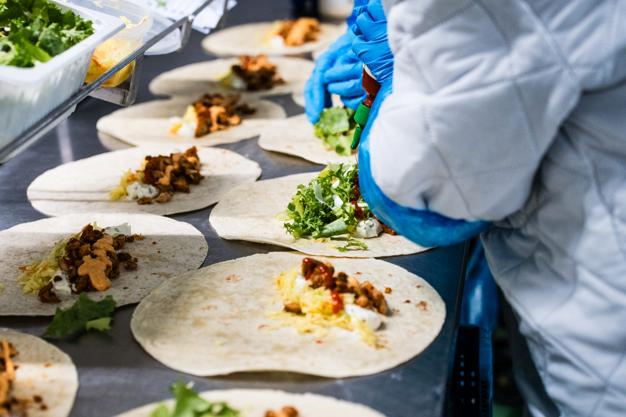 Belegte Tortillas in einer Reihe, eine Hand legt Salat auf