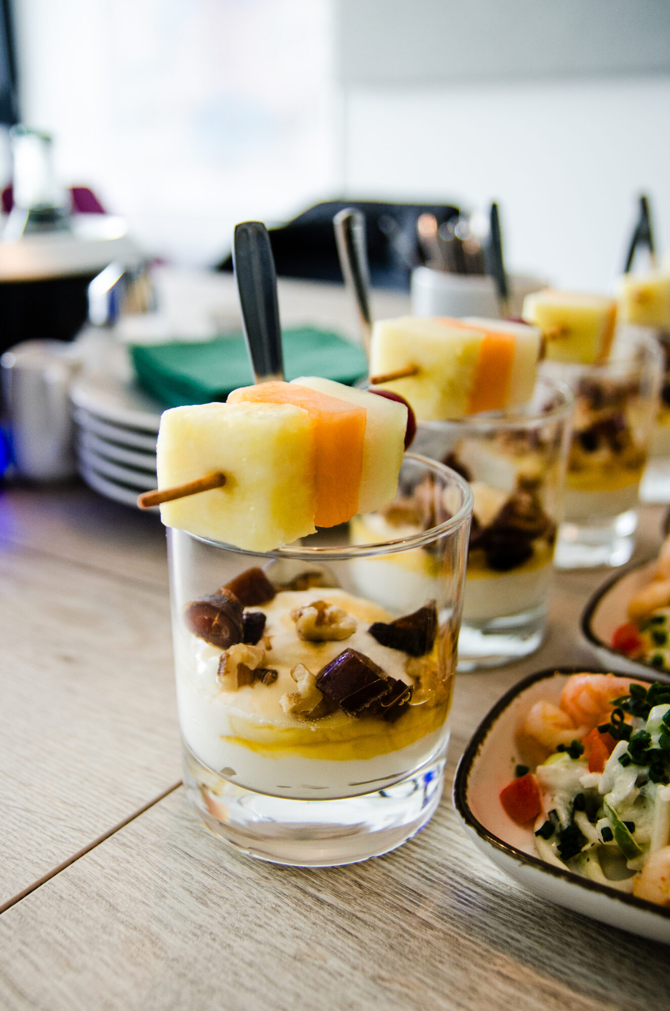 Dessertglas mit Fruchtspieß vor einer Reihe Fingerfood-Schalen